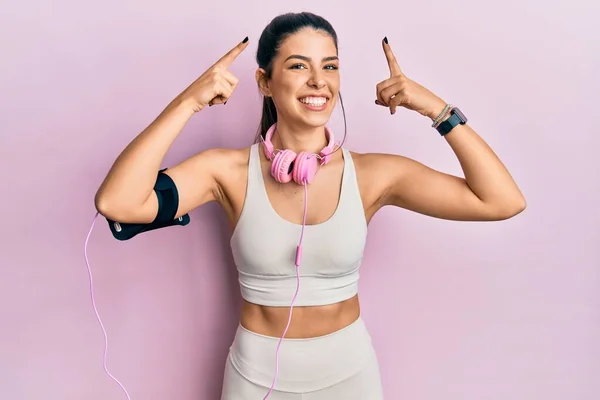 Young Hispanic Woman Wearing Gym Clothes Using Headphones Smiling Pointing — ストック写真