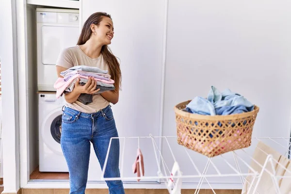 Young hispanic girl doing laundry holding folded clothes at home.
