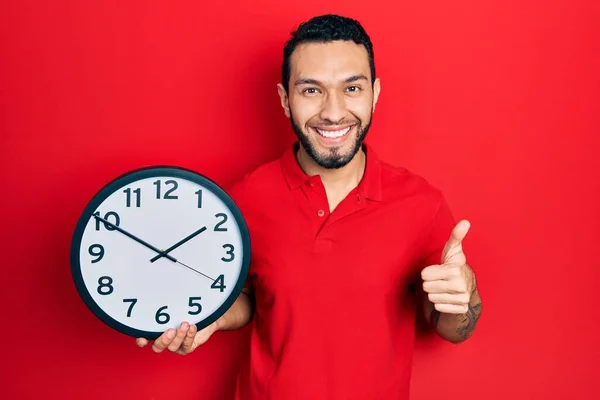 Hispanic Man Beard Holding Big Clock Smiling Happy Positive Thumb — Φωτογραφία Αρχείου