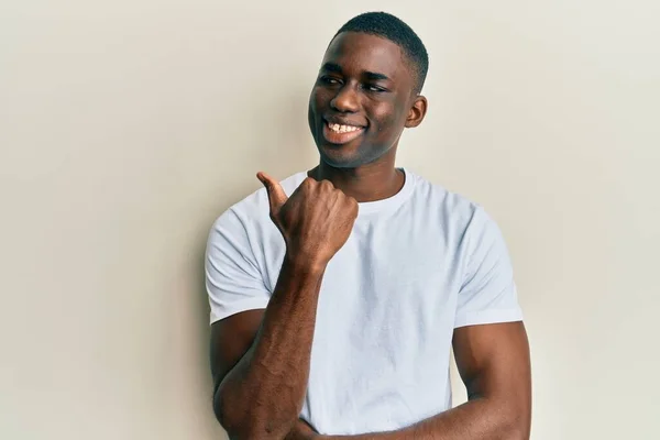 年轻的非洲裔美国人 身穿休闲的白色T恤 面带微笑 面带微笑 手指头指向旁边 — 图库照片