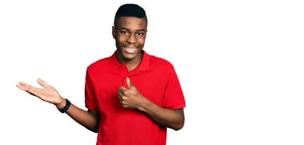 若いアフリカ系アメリカ人男性を着てカジュアルな赤いTシャツを示すヤシの手と親指で をジェスチャーを行います 笑顔幸せと陽気な — ストック写真