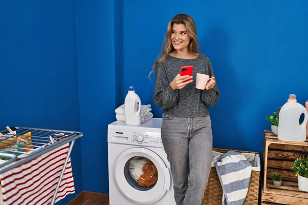 Ung Blond Kvinna Med Smartphone Och Dricka Kaffe Väntar Tvättmaskin — Stockfoto