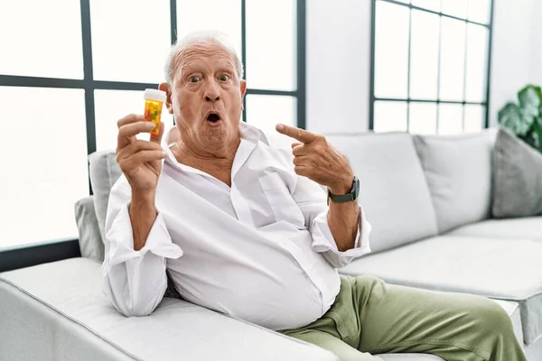 Senior Man Holding Pills Surprised Pointing Finger Side Open Mouth — Stock fotografie