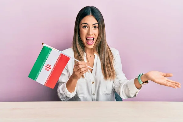 Young Hispanic Woman Holding Iran Flag Sitting Table Celebrating Achievement — Stock Photo, Image