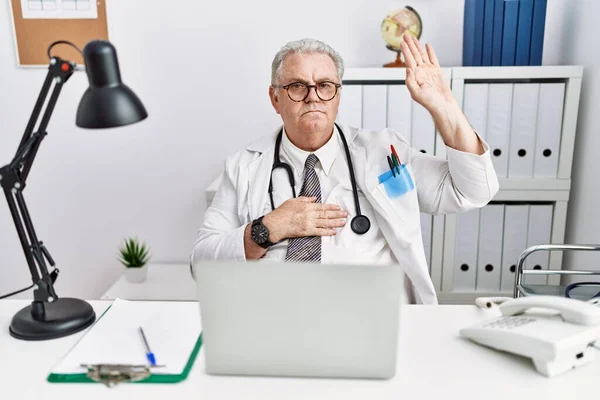 Senior caucasian man wearing doctor uniform and stethoscope at the clinic swearing with hand on chest and open palm, making a loyalty promise oath