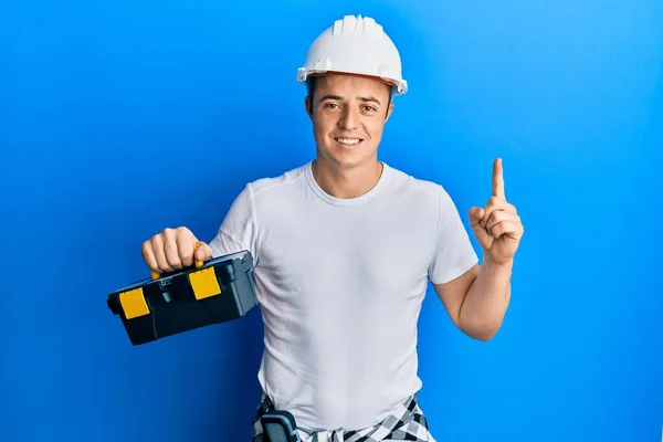 Bonito Jovem Usando Capacete Segurança Segurando Caixa Ferramentas Sorrindo Com — Fotografia de Stock