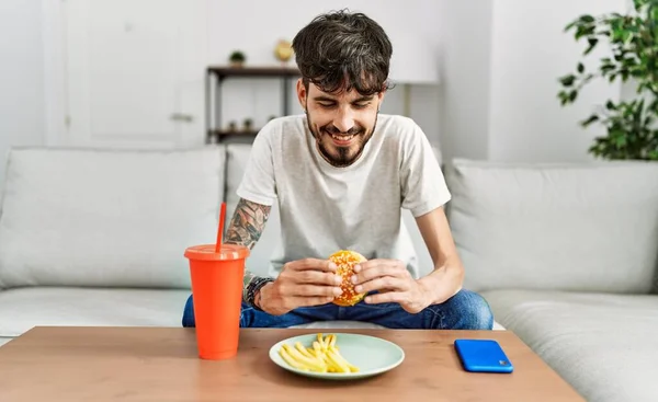 Ung Latinamerikan Äter Klassisk Hamburgare Och Dricker Läsk Sittandes Soffan — Stockfoto