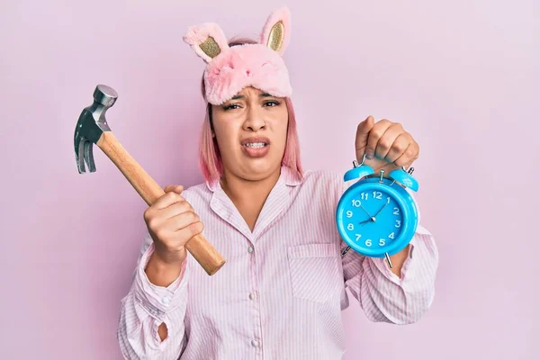 Hispanic Woman Pink Hair Wearing Pajama Holding Hammer Alarm Clock — Stockfoto