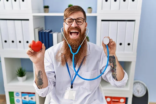 Redhead Man Long Beard Wearing Doctor Uniform Holding Heart Stethoscope — Zdjęcie stockowe