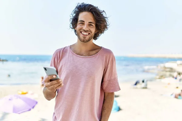 Ung Latinamerikansk Man Ler Glad Med Smartphone Stranden — Stockfoto