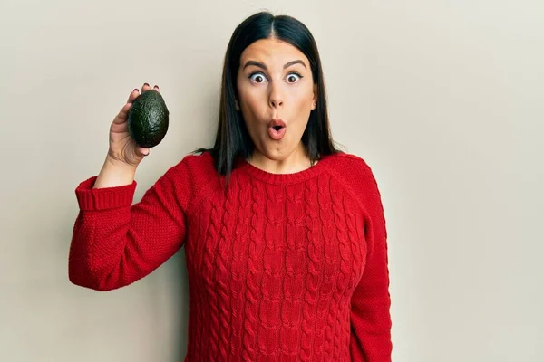 Beautiful Brunette Woman Holding Avocado Scared Amazed Open Mouth Surprise — Zdjęcie stockowe