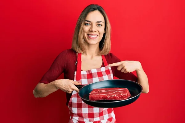 Νεαρή Καυκάσια Ξανθιά Γυναίκα Που Φοράει Μαγειρεμένη Ποδιά Μαγειρεύοντας Κρέας — Φωτογραφία Αρχείου