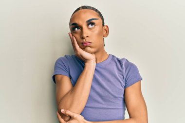 Hispanic man wearing make up and long hair wearing casual t shirt thinking looking tired and bored with depression problems with crossed arms. 