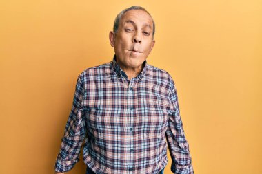 Handsome senior man with grey hair wearing casual shirt making fish face with lips, crazy and comical gesture. funny expression. 