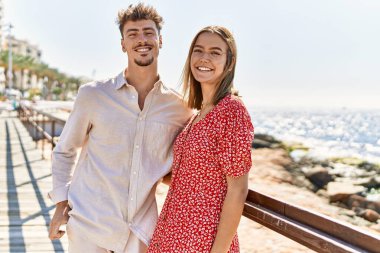 Genç İspanyol çift tatilde gülümsüyor ve sahilde birbirlerine sarılıyorlar.