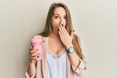 Sarışın genç bir kadın bir fincan kahve içerek ağzını eliyle kapatıyor, şok geçiriyor ve hata yapmaktan korkuyor. şaşırmış ifade 