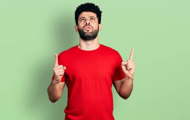 Gündelik kırmızı tişörtlü genç Arap adam şaşırdı ve şaşırdı. Parmaklarıyla işaret etti ve kollarını kaldırdı.. 