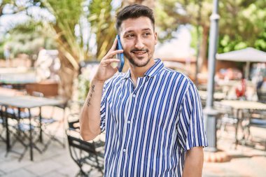 Genç yakışıklı adam parkta telefonla konuşuyor.