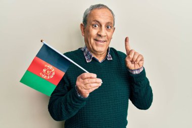 Handsome senior man with grey hair holding afghanistan flag smiling with an idea or question pointing finger with happy face, number one 