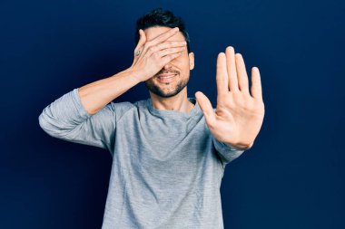 Latin kökenli genç bir adam, günlük kıyafetler giyip, elleriyle gözlerini kapatıyor ve üzgün ve korku ifadeleriyle jestleri durduruyor. utangaç ve olumsuz kavram. 