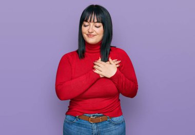 Gündelik kıyafetler giyen genç İspanyol kadın elleri göğsünde, gözleri kapalı ve yüzünde minnet dolu bir jest ile gülümsüyor. sağlık kavramı. 