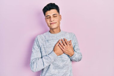 Gündelik kıyafetler giyen genç İspanyol adam elleri göğsünde, gözleri kapalı ve yüzünde minnet dolu bir jest ile gülümsüyor. sağlık kavramı. 