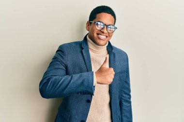 Zarif kıyafetler ve gözlük takan genç, yakışıklı İspanyol adam elleriyle mutlu bir jest yapıyor. Kameraya bakıp başarıyı gösteren ifade. 