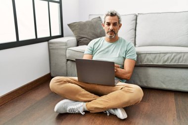 Orta yaşlı İspanyol bir adam oturma odasında dizüstü bilgisayar kullanıyor. Uykulu ve yorgun görünüyor. Yorgun ve akşamdan kalma, tembel gözleri var.. 