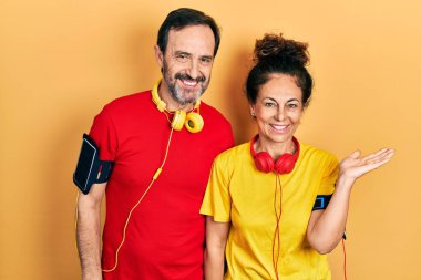 Middle age couple of hispanic woman and man wearing sportswear and arm band smiling cheerful presenting and pointing with palm of hand looking at the camera. 