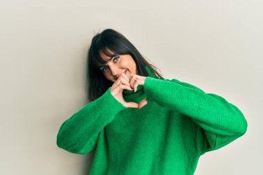 Gündelik bir kazak giyen genç İspanyol kadın. Sevgiyle gülümsüyor. Elleriyle kalp sembolü ve şekli gösteriyor. romantik kavram. 