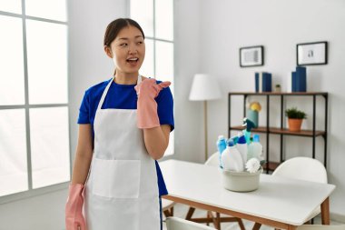 Daha temiz bir üniforma giyen genç Çinli kız mutlu bir yüzle gülümseyerek başparmağıyla yan tarafı işaret ediyor.. 