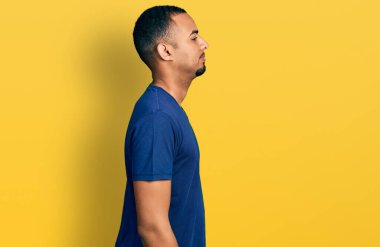 Young african american man wearing casual t shirt looking to side, relax profile pose with natural face with confident smile. 