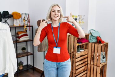 Young caucasian woman working as manager at retail boutique smiling cheerful showing and pointing with fingers teeth and mouth. dental health concept. 