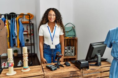 Güzel İspanyol kadın giyim mağazasında çalışıyor. Pozitif ve mutlu görünüyor. Duruyor ve gülümsüyor. 