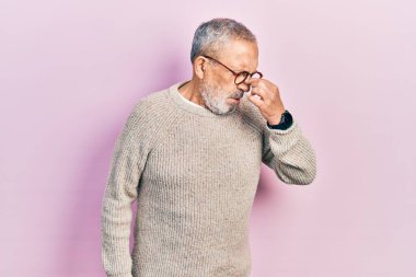 Handsome senior man with beard wearing casual sweater and glasses tired rubbing nose and eyes feeling fatigue and headache. stress and frustration concept. 