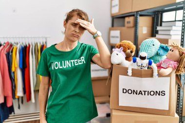 Beautiful caucasian woman wearing volunteer t shirt at donations stand worried and stressed about a problem with hand on forehead, nervous and anxious for crisis 