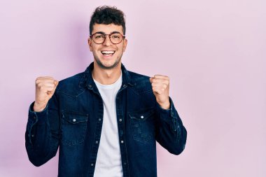 Gündelik kıyafet ve gözlük takan genç İspanyol adam kollarını kaldırıp, gözlerini açarak başarının şokunu yaşıyor ve hayrete düşüyor. Kazanan konsept. 