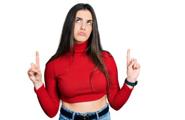 Kırmızı balıkçı yaka kazak giyen genç, üzgün ve üzgün görünüyor, parmaklarıyla yönü gösteriyor, mutsuz ve depresif.. 