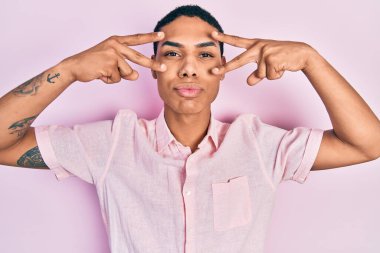 Genç Afrikalı Amerikalı adam zafer işareti ve barış jesti yapıyor. Kameraya bakıp öpüşürken sevimli ve seksi görünüyor. aşk ifadesi. 