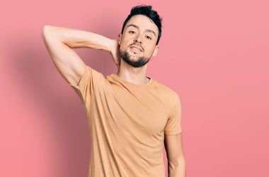 Sakallı, sıradan tişörtlü, boynu ağrıyan, eliyle boynuna dokunan, kas ağrısı çeken İspanyol bir adam. 