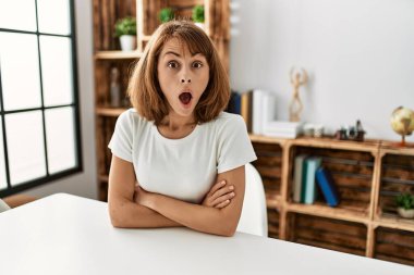 Young caucasian girl wearing casual clothes sitting on the table at home afraid and shocked with surprise expression, fear and excited face. 