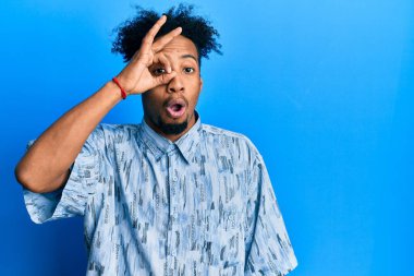 Young african american man with beard wearing casual clothes doing ok gesture shocked with surprised face, eye looking through fingers. unbelieving expression. 