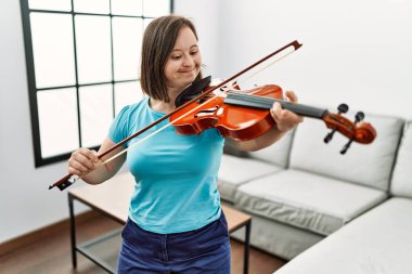 Down sendromlu esmer kadın oturma odasında keman çalışıyor.