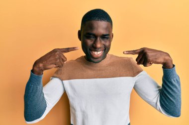 Gündelik kıyafetler giyen, neşeli gülümseyen, parmaklarıyla ve ağzıyla işaret eden Afrikalı genç bir Amerikalı. diş sağlığı kavramı. 
