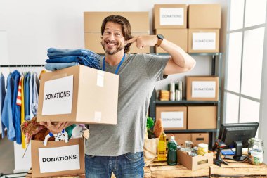 Handsome middle age man holding donations box for charity at volunteer stand smiling cheerful showing and pointing with fingers teeth and mouth. dental health concept. 