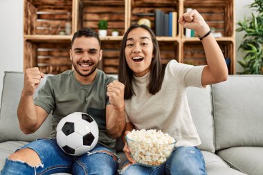 Genç latin çift evde futbol maçı izleyip porpcorn yiyorlar..