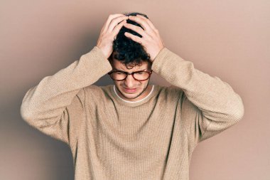 Günlük kıyafetler ve gözlük takan genç İspanyol adam baş ağrısı ve stres yüzünden acı çekiyor çünkü acı ve migren. Eller başının üstünde.. 