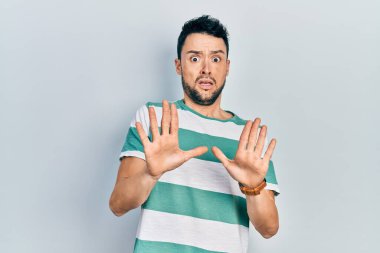 Günlük giysiler giyen genç İspanyol adam korku ifadesinden korkuyor ve dehşete düşüyor. El hareketlerini durdur, şok içinde bağır. panik konsepti. 