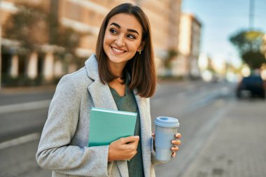 Genç İspanyol kız gülümsüyor, elinde kahve ve kitapla..