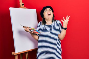 Orta yaşlı İspanyol kadın palet üstüne palet çizerek ayakta duruyor deli gibi bağırıyor ve agresif bir ifade ve kollarla bağırıyor. hüsran kavramı. 